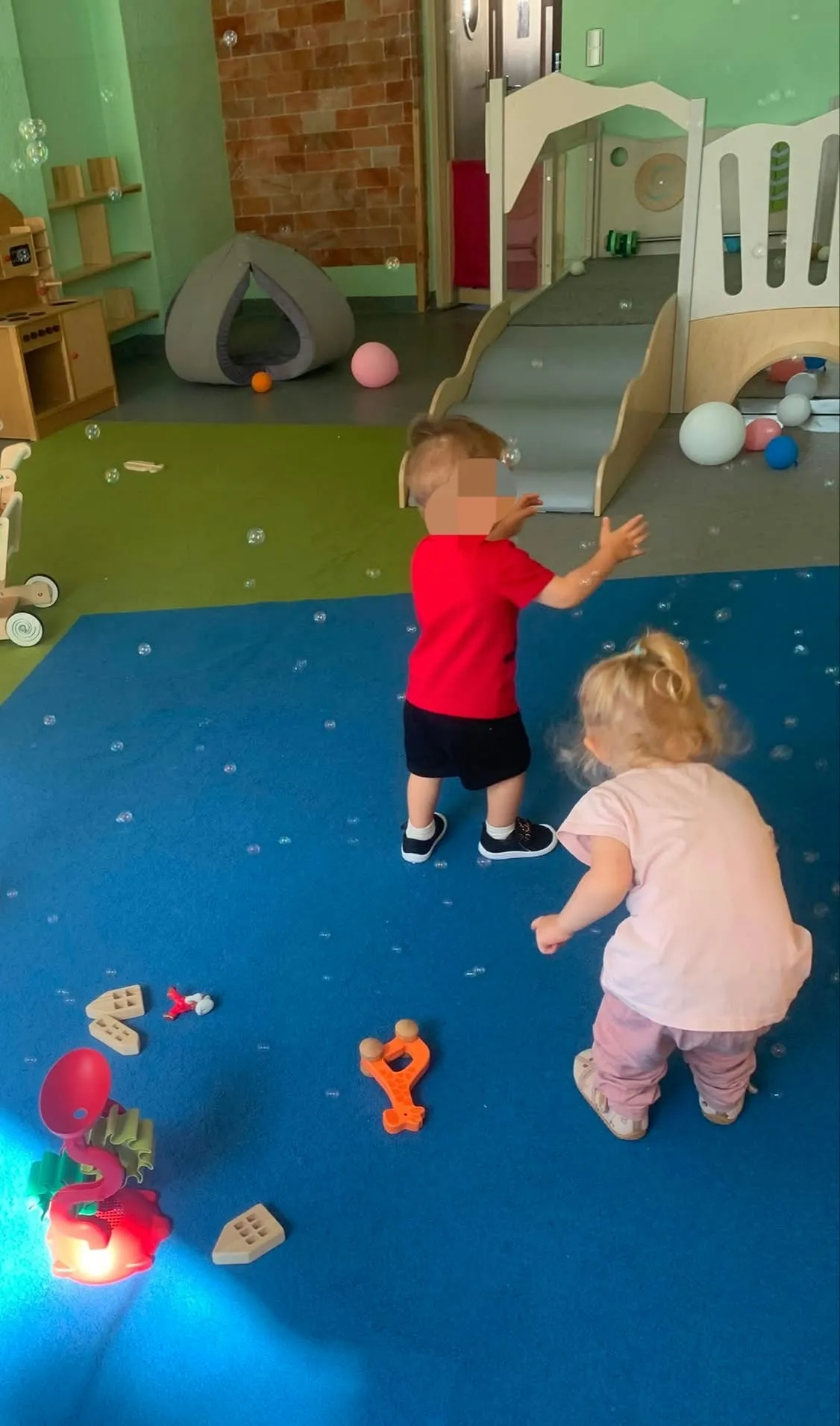 Dwoje dzieci bawi się bańkami mydlanymi w sali z drewnianymi konstrukcjami