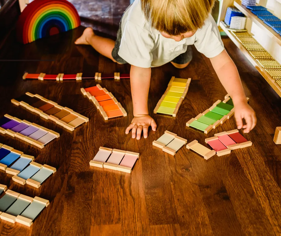 Dziecko układające kolorowe tabliczki Montessori na drewnianej podłodze – zajęcia sensoryczne w żłobku FreeDom Nursery we Wrocławiu
